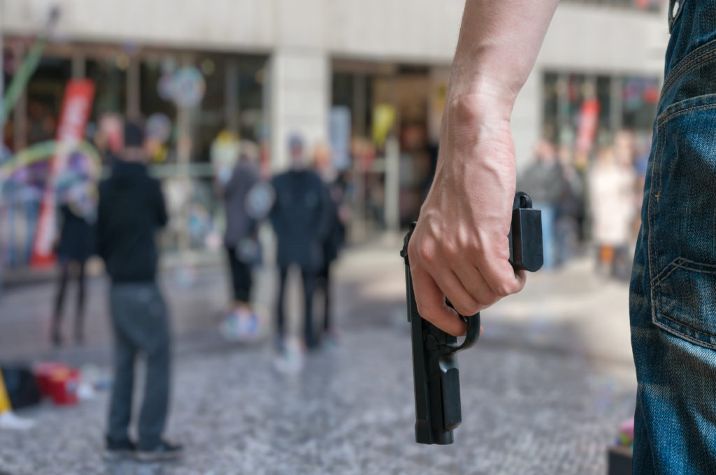 man with a gun facing a crowd of people in a shopping area or shopping mall