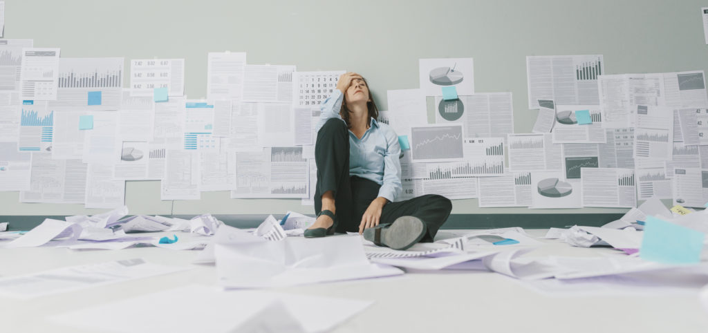 distressed business person sitting against wall surrounded by papers